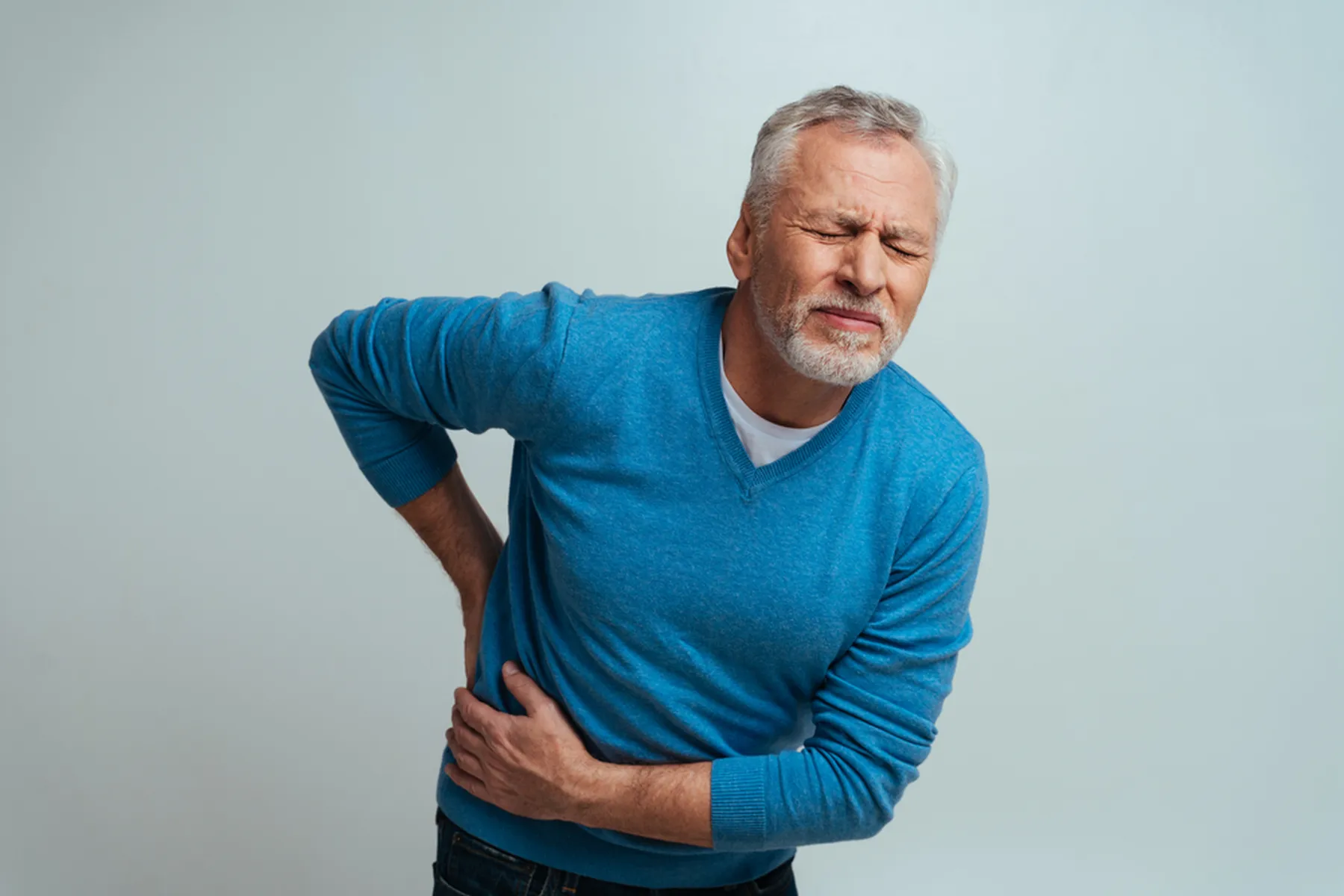 A man in a blue shirt clutches his lower abdomen in pain.