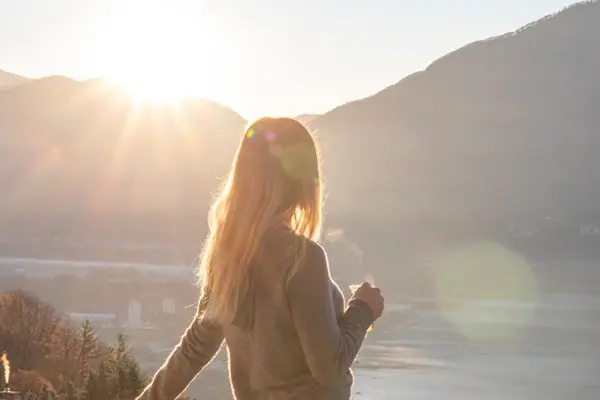 Woman standing on a balcony looking at the sun.