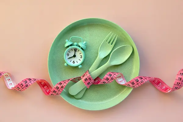A green plate with an alarm, fork, and knife on it and a tape measure.