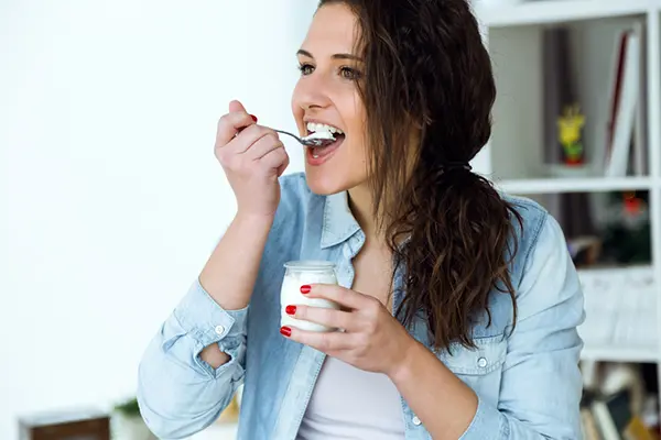 A woman eats yogurt and smiles.