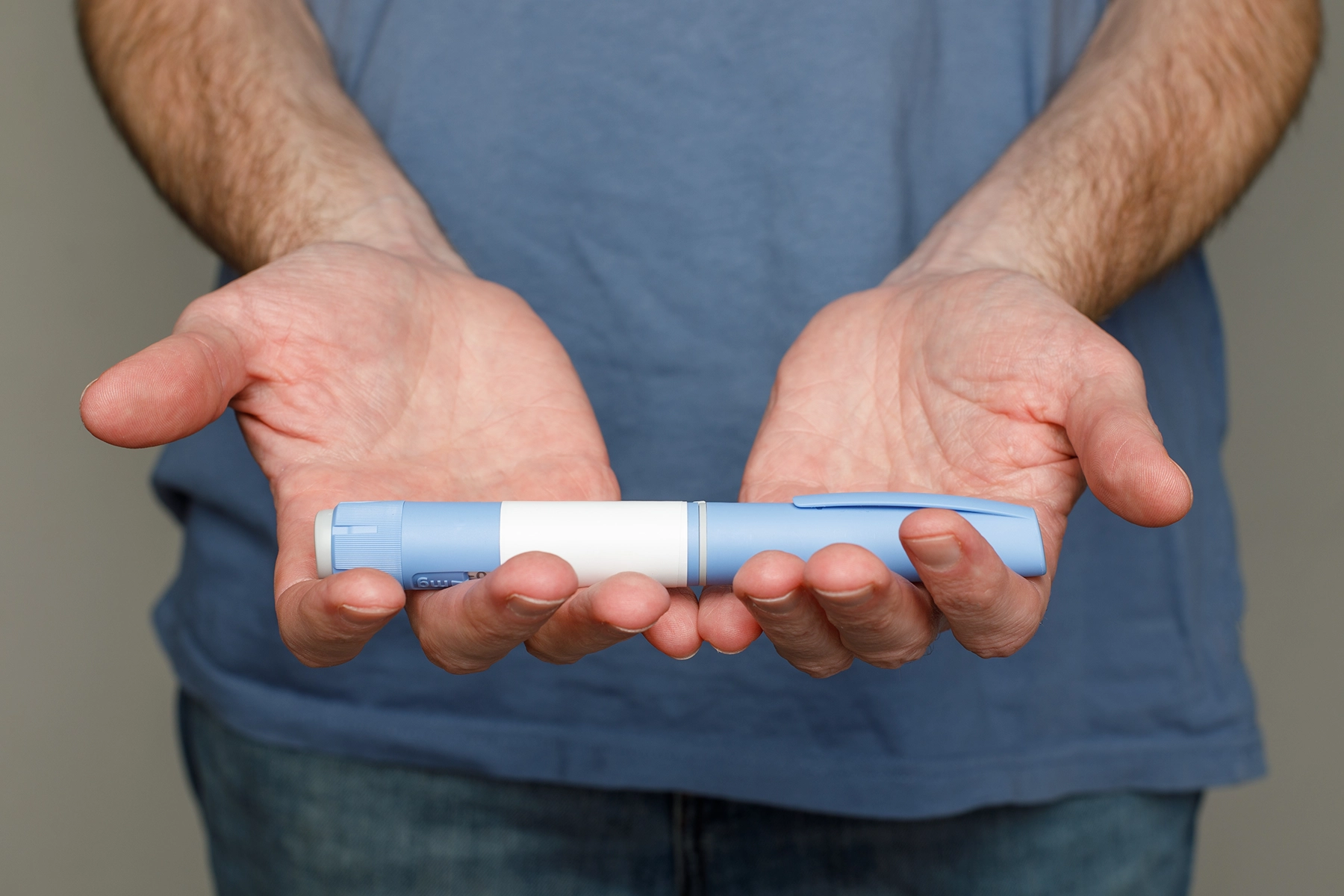 Man holding a GLP-1 pen in both hands
