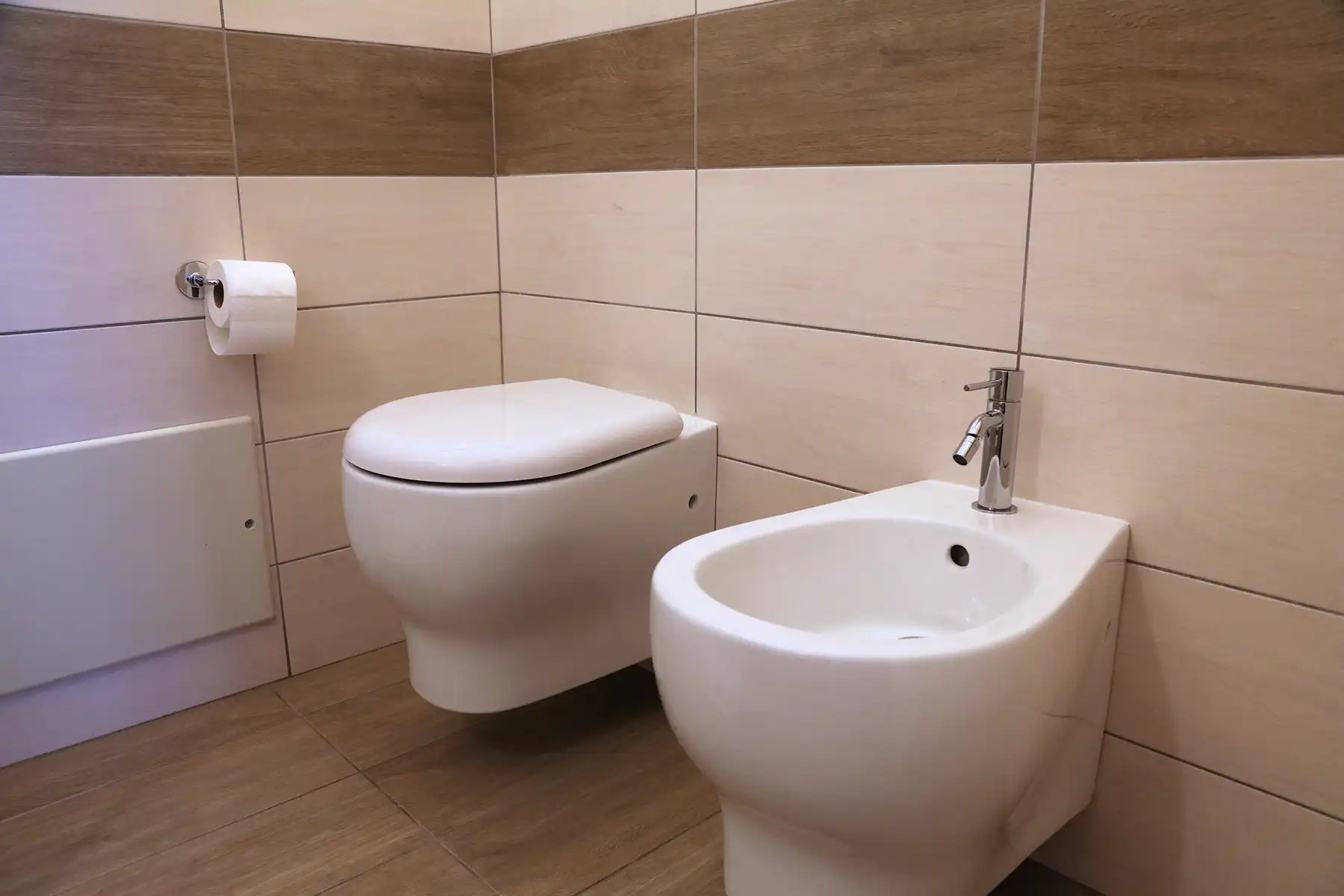 A toilet, a bidet, and toilet paper  in the bathroom.