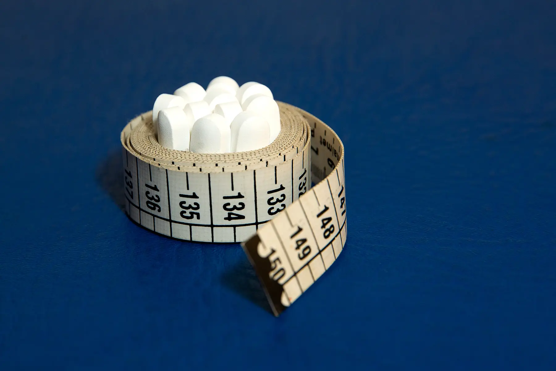 Tape measure wrapped around several appetite suppressant pills.