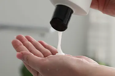 Mano recibiendo una porción de shampoo blanco desde un dispensador Mano recibiendo una porción de shampoo blanco desde un dispensador