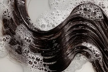 Primer plano de cabello oscuro y ondulado cubierto de espuma de shampoo Primer plano de cabello oscuro y ondulado cubierto de espuma de shampoo