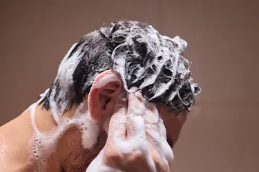 Persona lavándose el cabello con espuma cerca de la oreja, vista desde atrás Persona lavándose el cabello con espuma cerca de la oreja, vista desde atrás