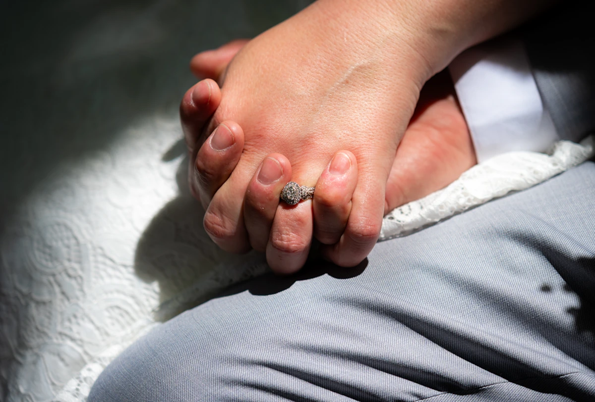 Bride and groom holding hands with the engagement ring illuminated by the sun.
