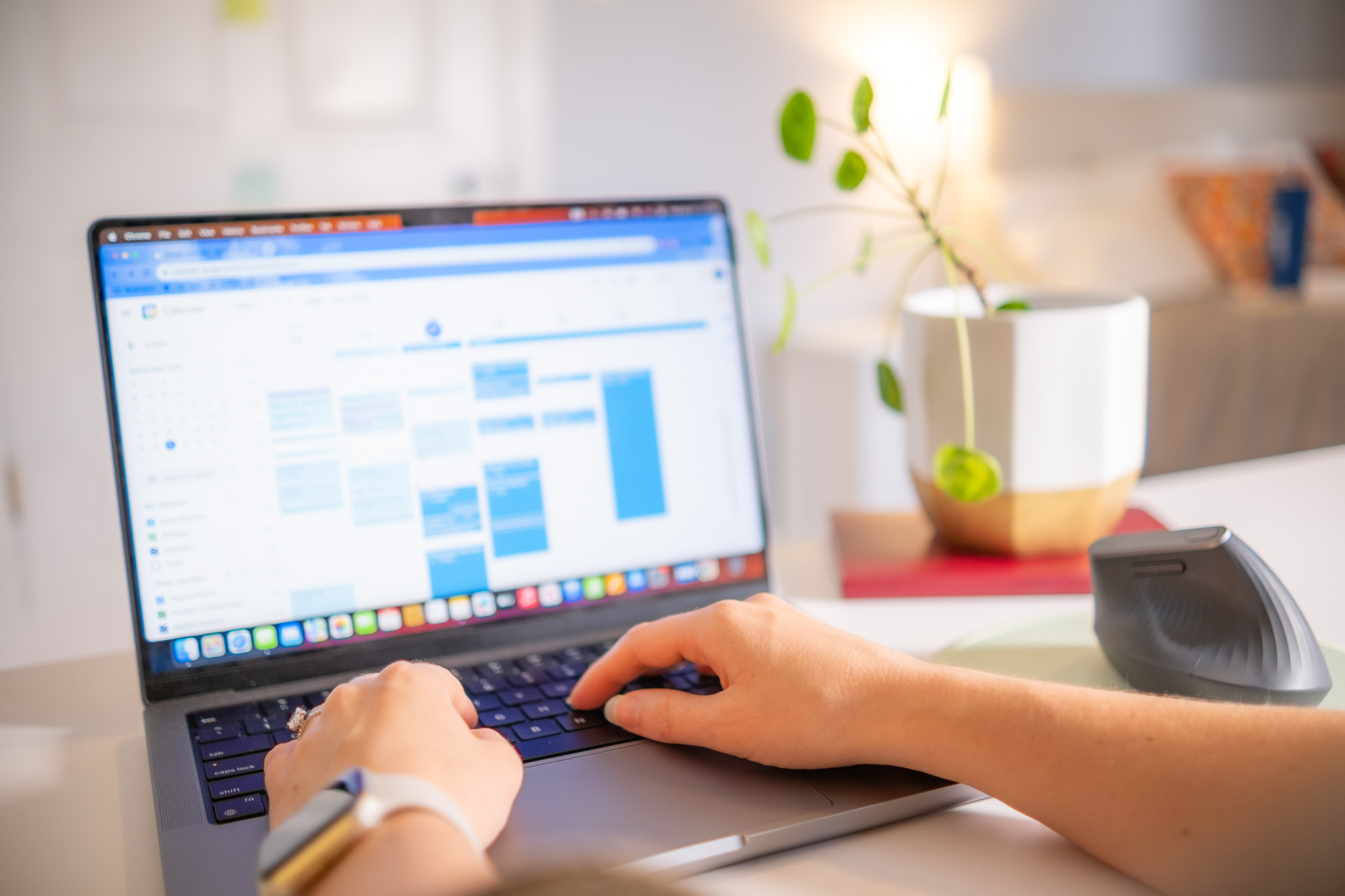 A person's hands typing on a laptop in a home office.