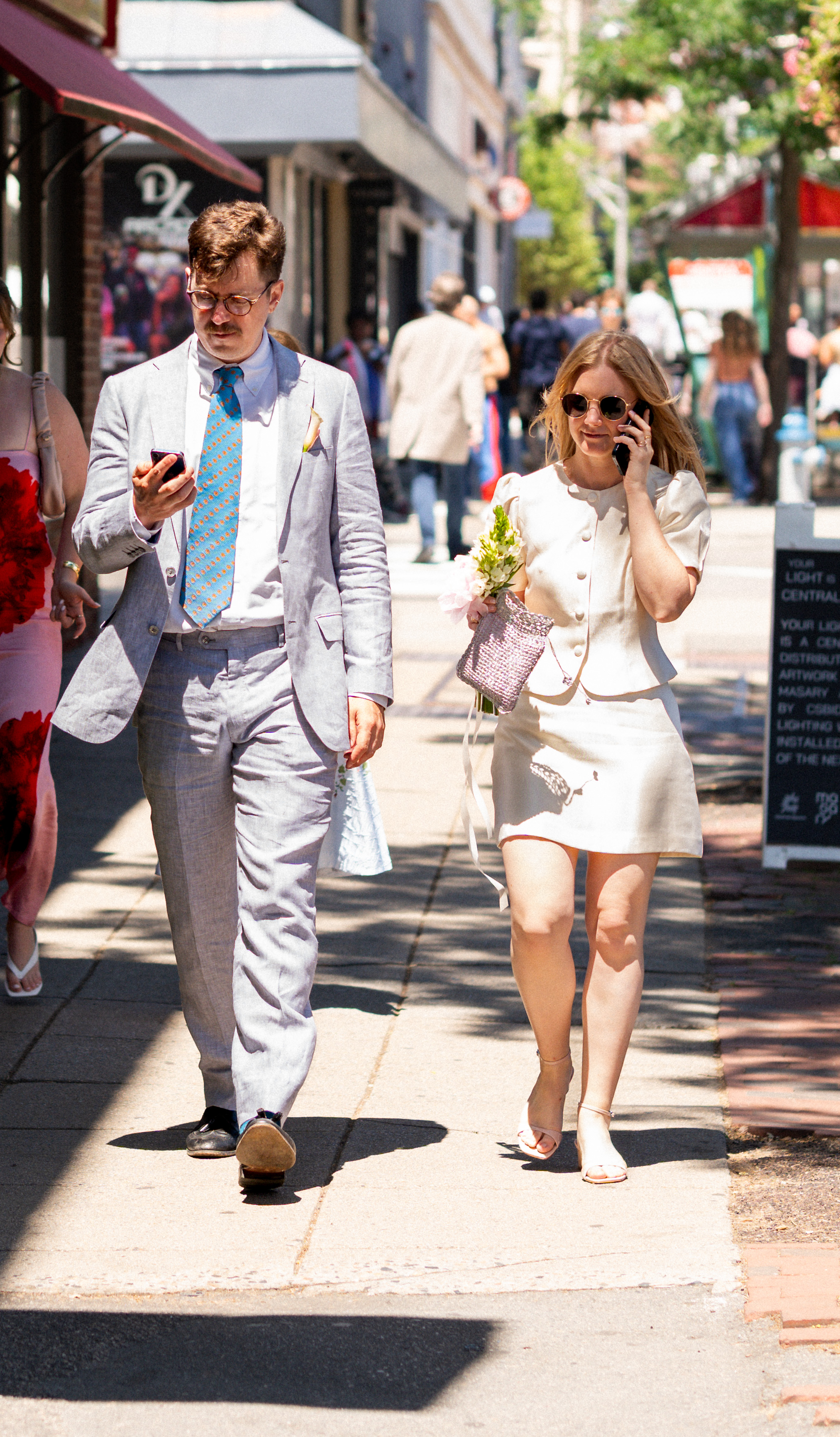 Bride and groom walking with phones in Central Square, Cambridge Massachusetts.