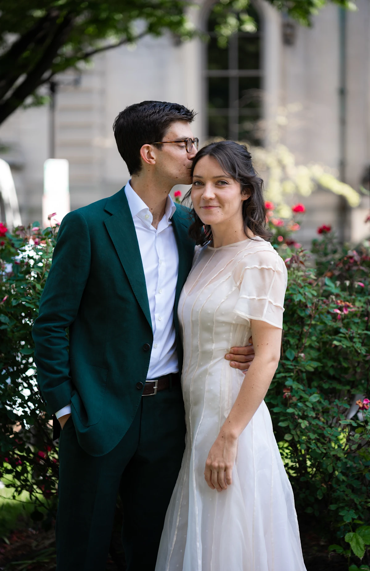 A groom kisses his bride's head as they pose.
