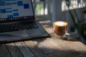 Outdoor table with a laptop and a latte on a sunny morning