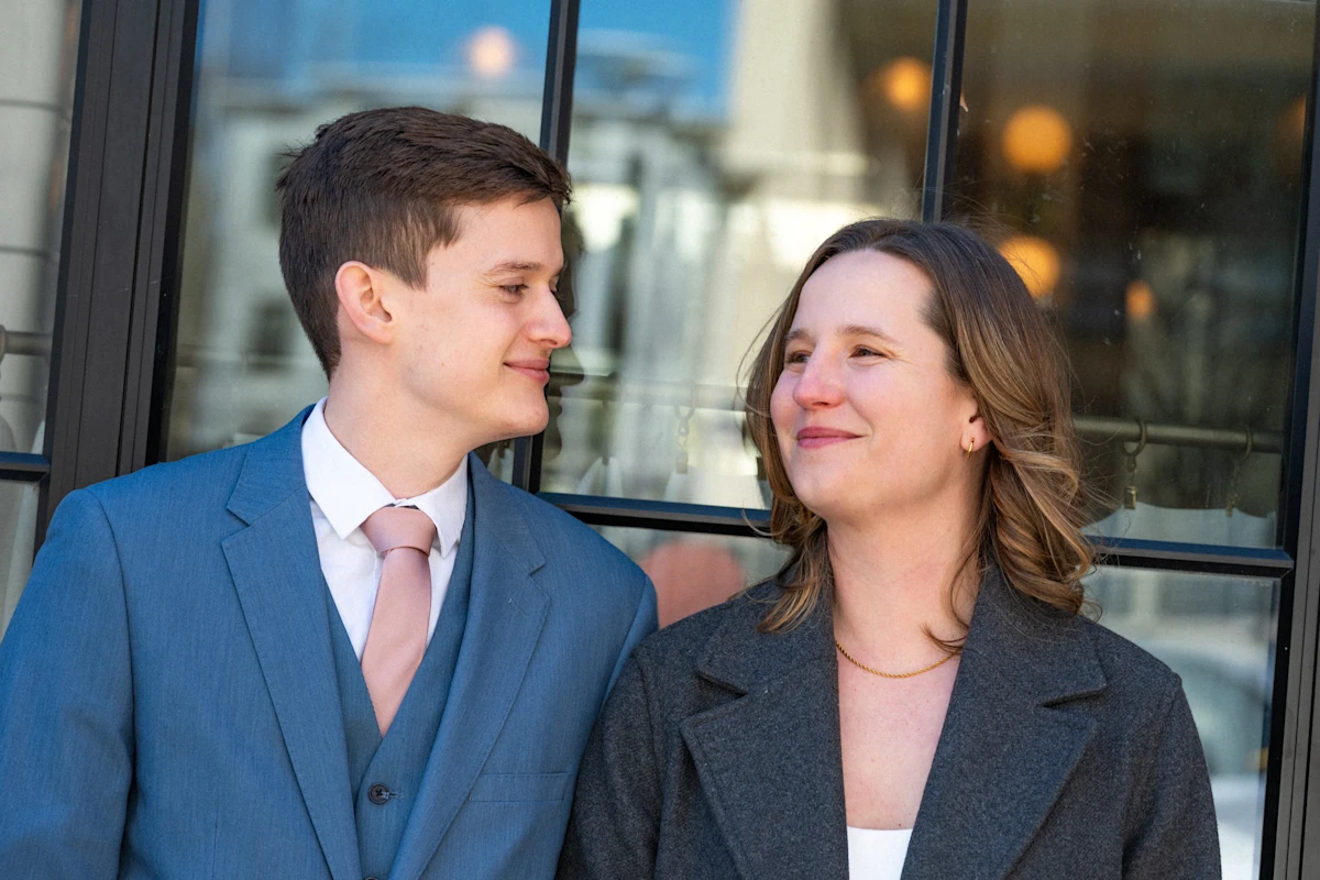 Groom smiling at bride as they hang out in front of a large window.
