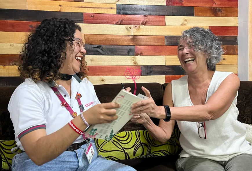 Emma Lucía Ardila sobre el lado izquierdo y mujer sobre la derecha, ríen mientras Emma le entrega el libro a la mujer después de firmarlo