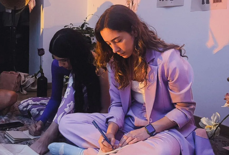 Luisa Montoya, sentada en el piso, escribe en una libreta. 