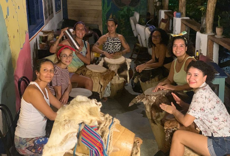 Siete mujeres están sentadas mirando a la cámara posando con tambores e instrumentos musicales.
