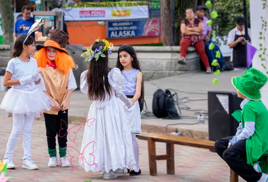 Cinco niños en escena de la obra "Alicia en el país de los números", una adaptación de la obra de Lewis Carroll. El sombrerero habla con el conejo y Alicia mira preocupada a la Reina Blanca. El quinto niño tiene un sombrero y su rostro no es visible