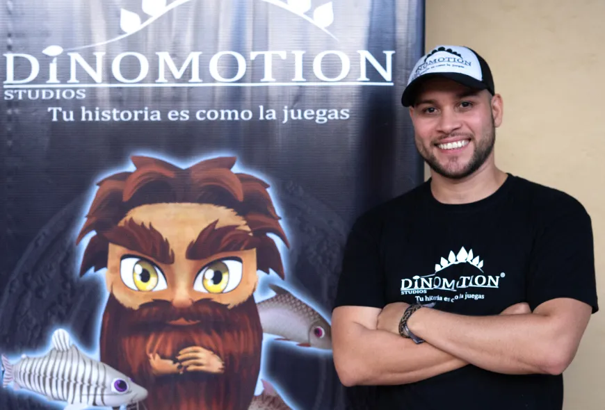 Holman Zarate posa al lado de una imagen del publicidad del videojuego El Mohán.