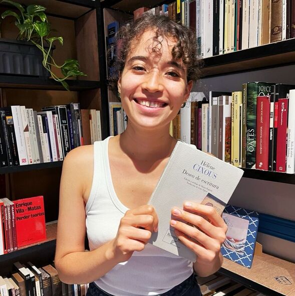 Manuela Montoya, librera de Los Caballitos del Diablo, sonríe a la cámara, sosteniendo una copia de "Deseo de Escritura", de la autora francesa Hélène Cixous.