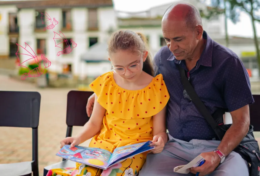 Un hmbre sin cabello sobre el lado derecho sostiene un papel con una mano y con la otra rodea a su hija, quien sostiene un libro. Ambos leen en silencio el cuento.