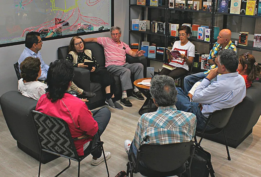 Diez personas están reunidas. Están organizados en circulo y todos están sentados. Algunos sostienen libros. Una de las personas está hablando, los demás lo escuchan. 