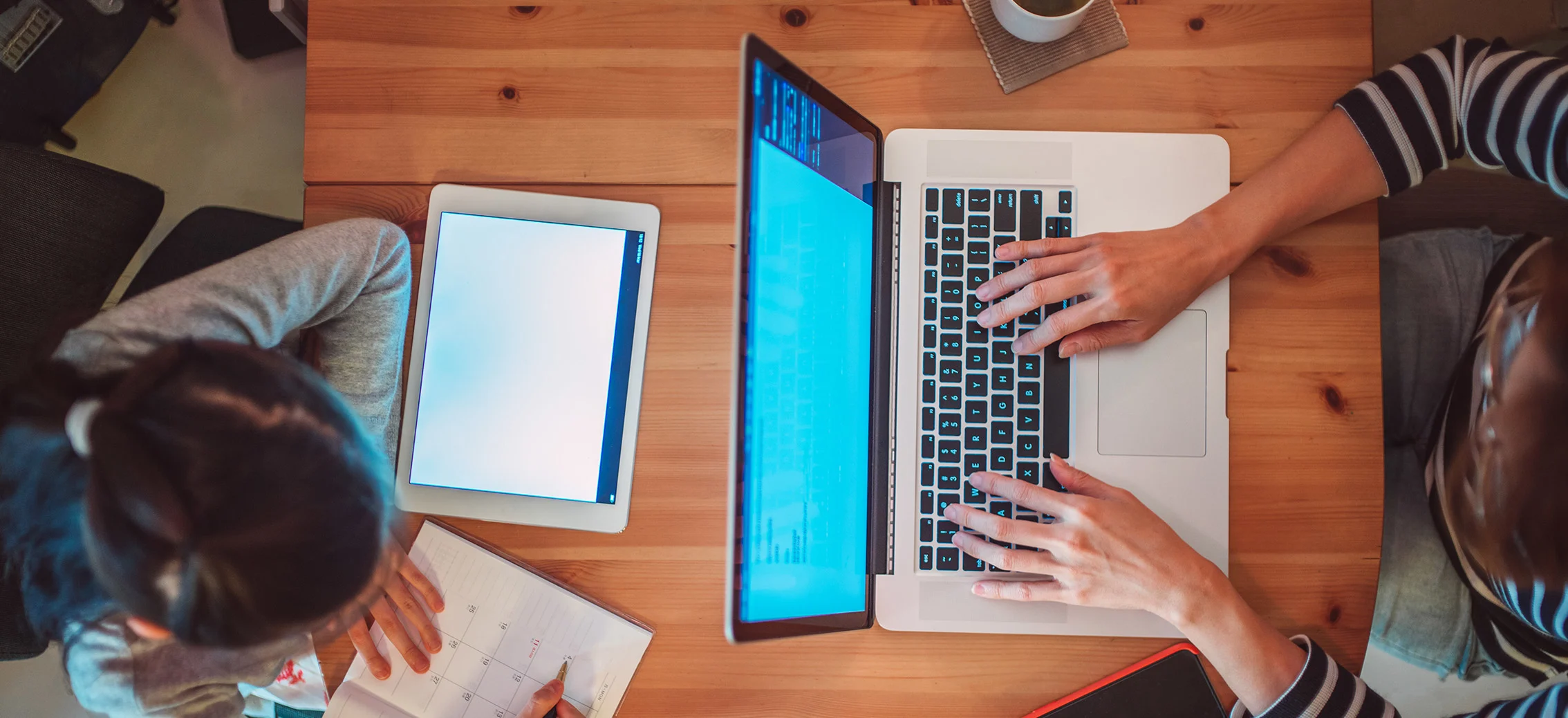 Parent on laptop, child on tablet at the table