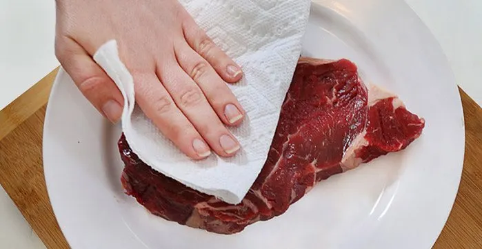 Woman patting steak dry with a Bounty paper towel sheet