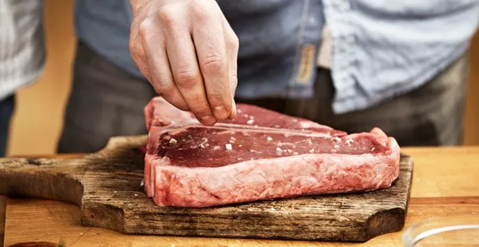 Man salting a steak on top of a wooden cutting board