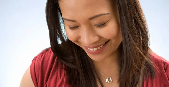 Woman looking down smiling while wearing a silver necklace