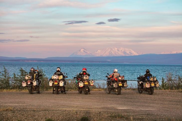 Motorcycles lined up looking over a lake with mountains in the distance