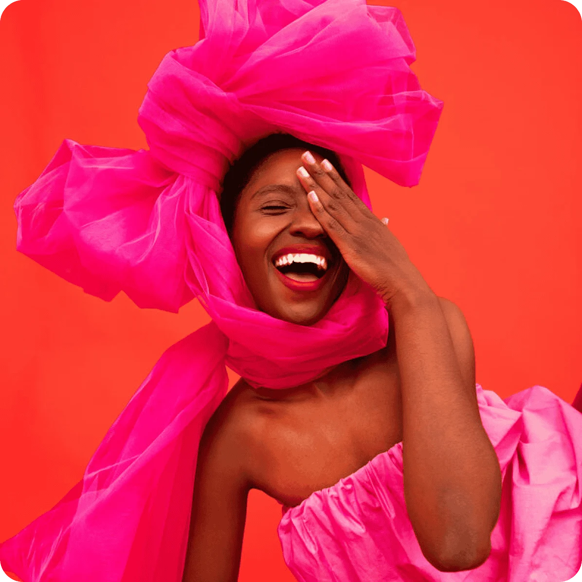 Woman smiling and covering one eye, wearing a pink dress and and an oversized pink bow on her head