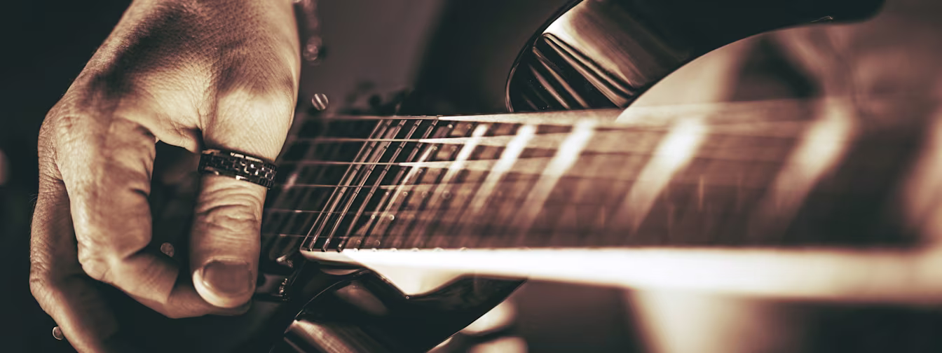 Hand zupft die Saiten einer Rock Gitarre