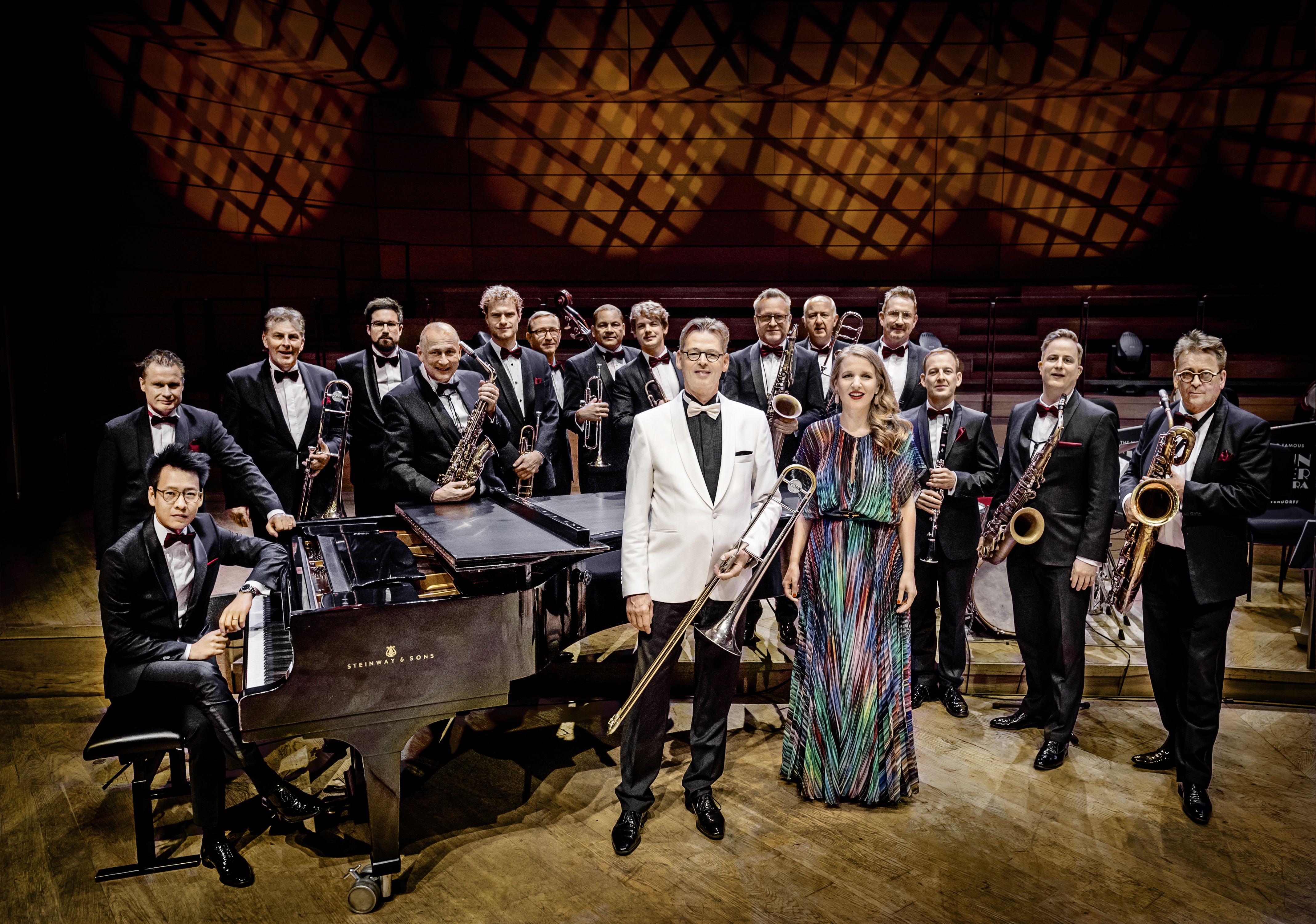 Big Band mit Bläsern, Klavier und Dirigentin in festlicher Konzertsaal-Atmosphäre