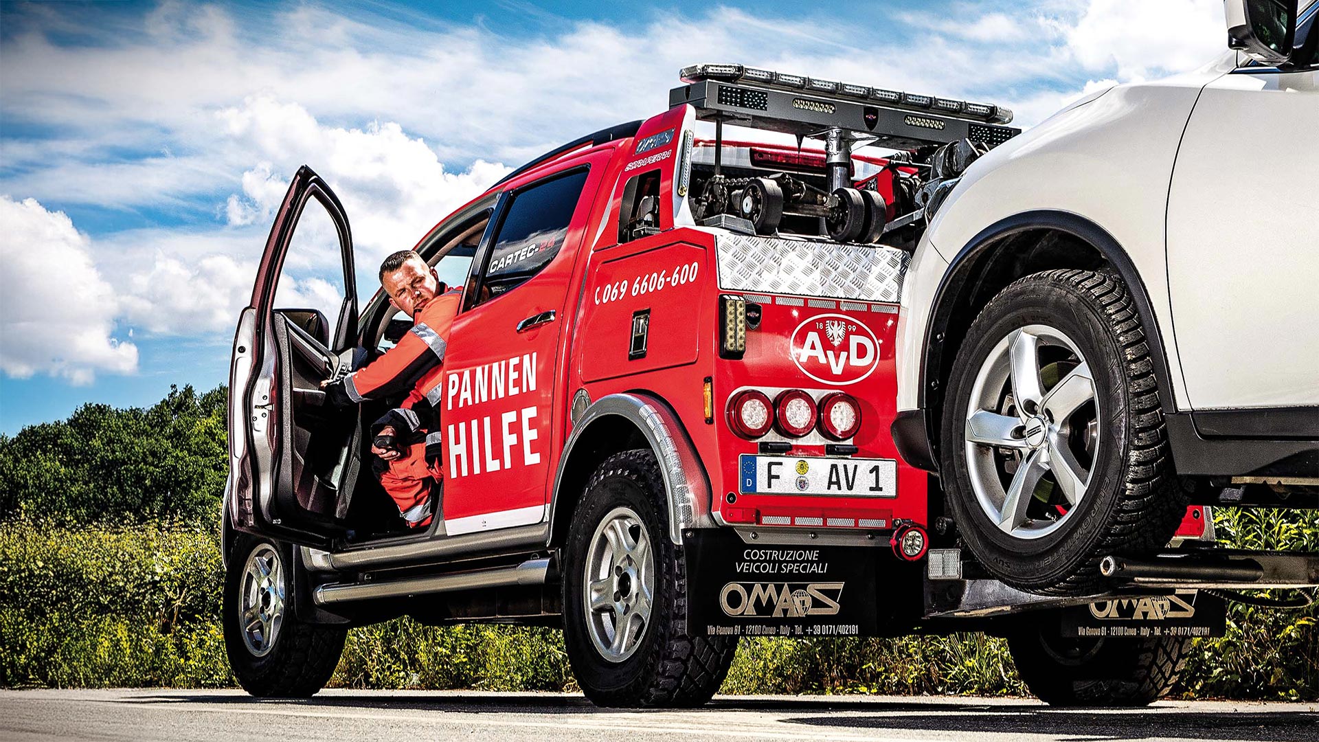 Pannenhilfefahrzeug mit offenem Fahrerhaus hilft einem weißen Auto am Straßenrand