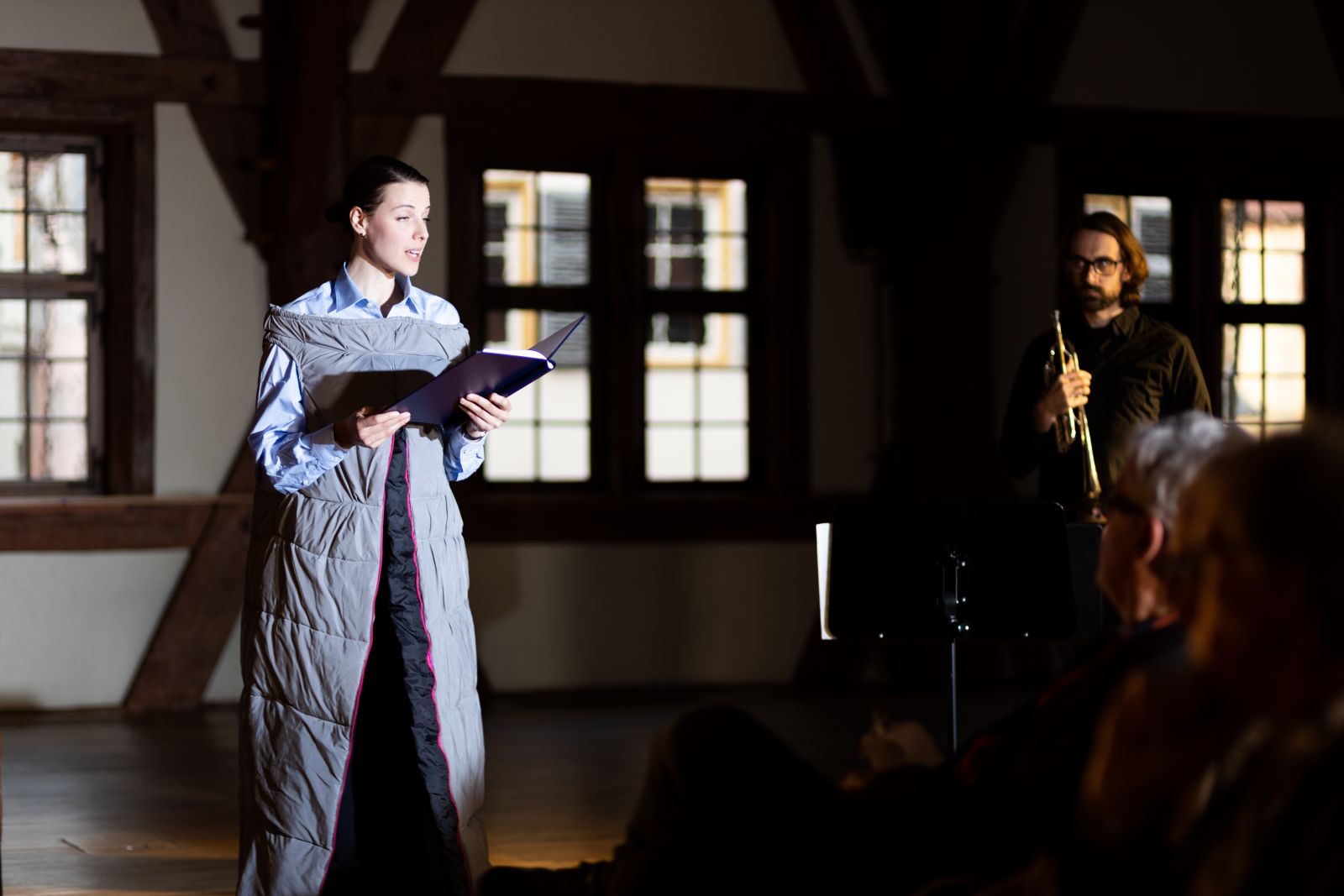 Frau in stehend erzählt, Musiker steht daneben, die Vorstellung "Maskenball" 2022 beim Podium Esslingen 