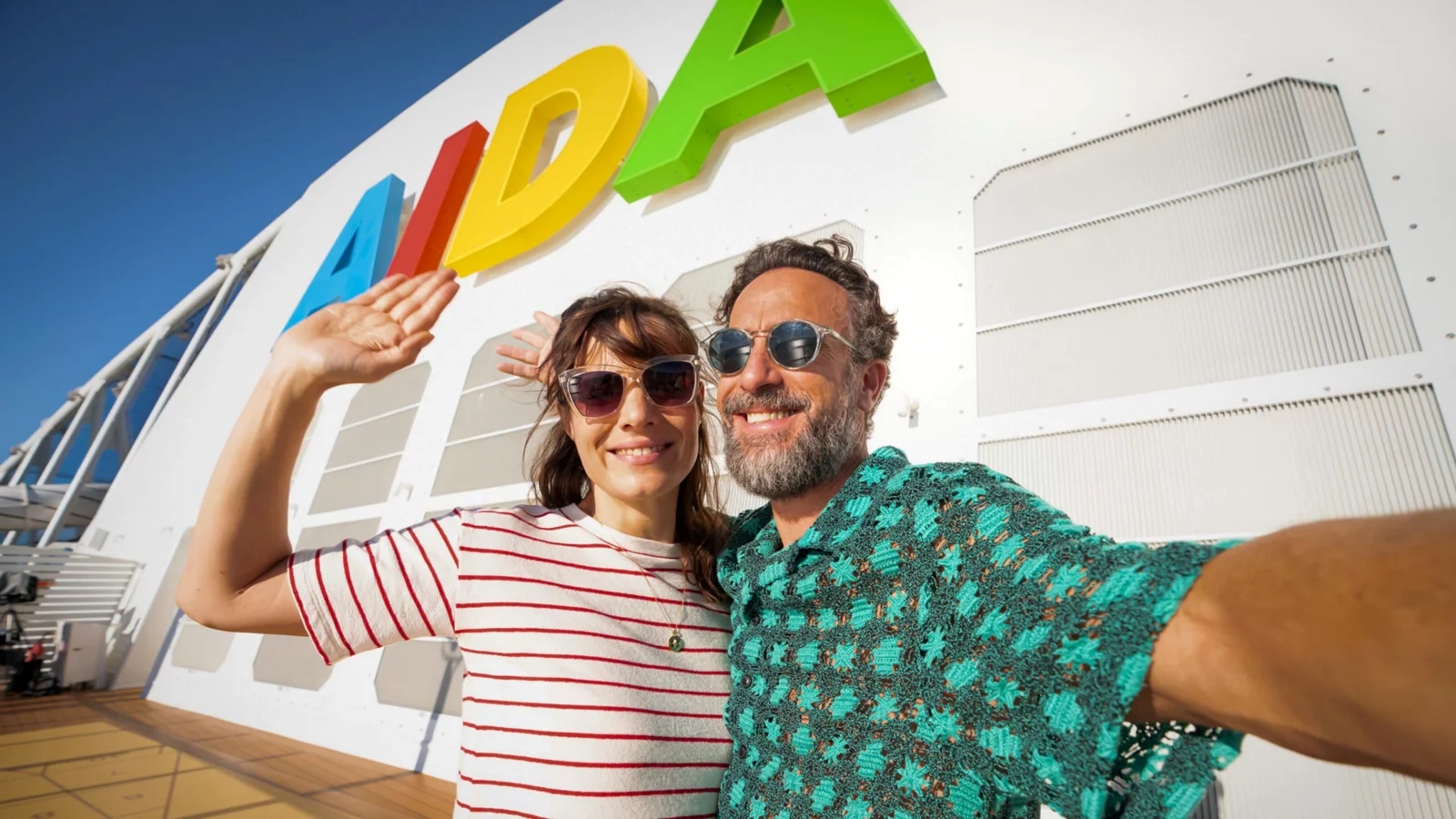 Zwei Personen posieren vor dem bunten AIDA-Schriftzug auf einem Kreuzfahrtschiff