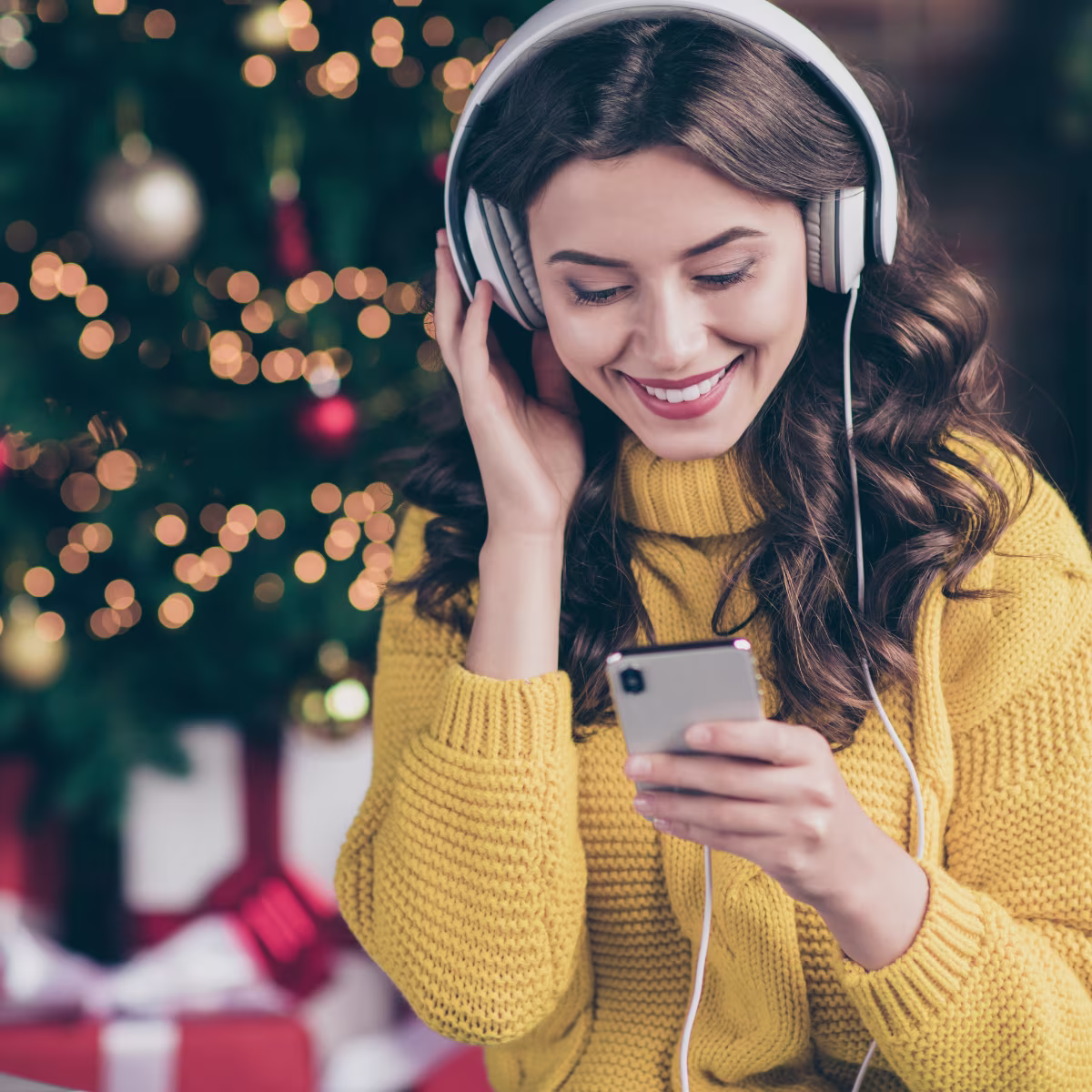Frau hört über Kopfhörer vorm Weihnachtsbaum Musik