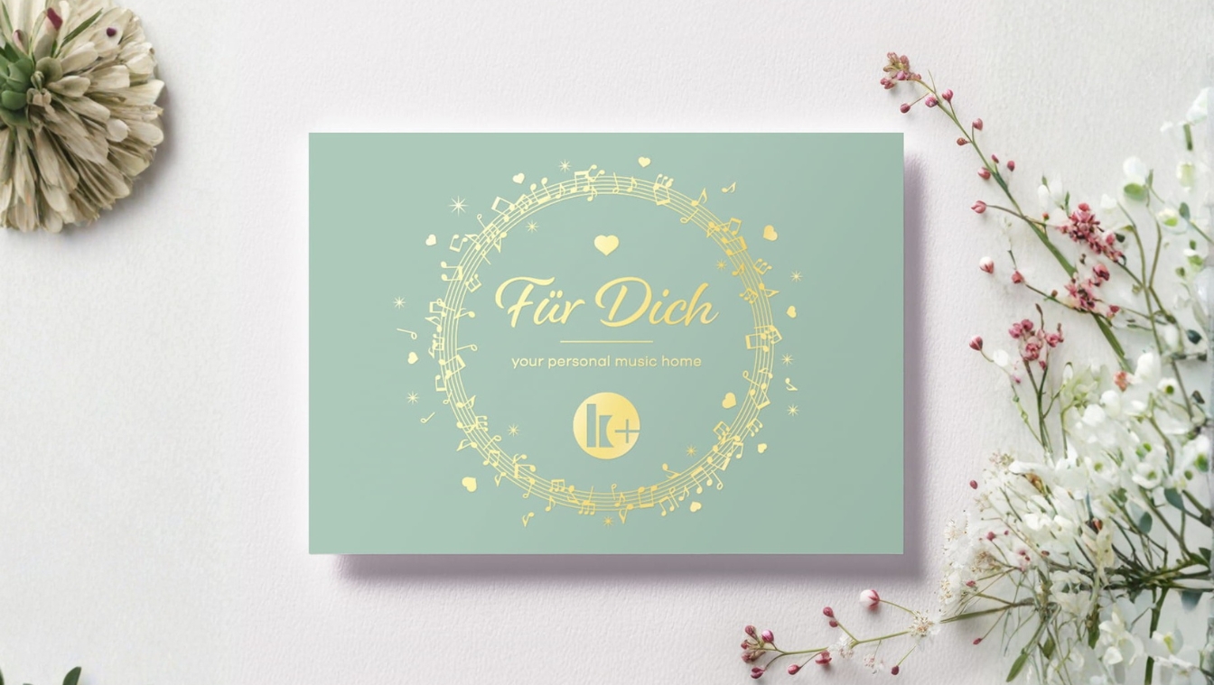 Grüne Karte mit goldenen Noten, Herzen und dem Schriftzug „Für Dich“ zwischen Blumen.