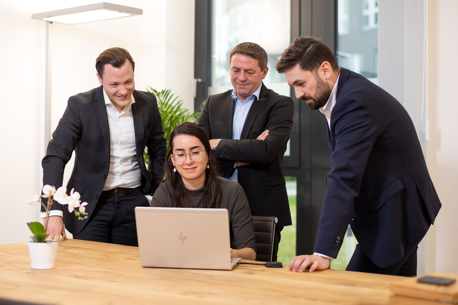Vier Personen im Business-Outfit arbeiten gemeinsam an einem Laptop in einem modernen Büro