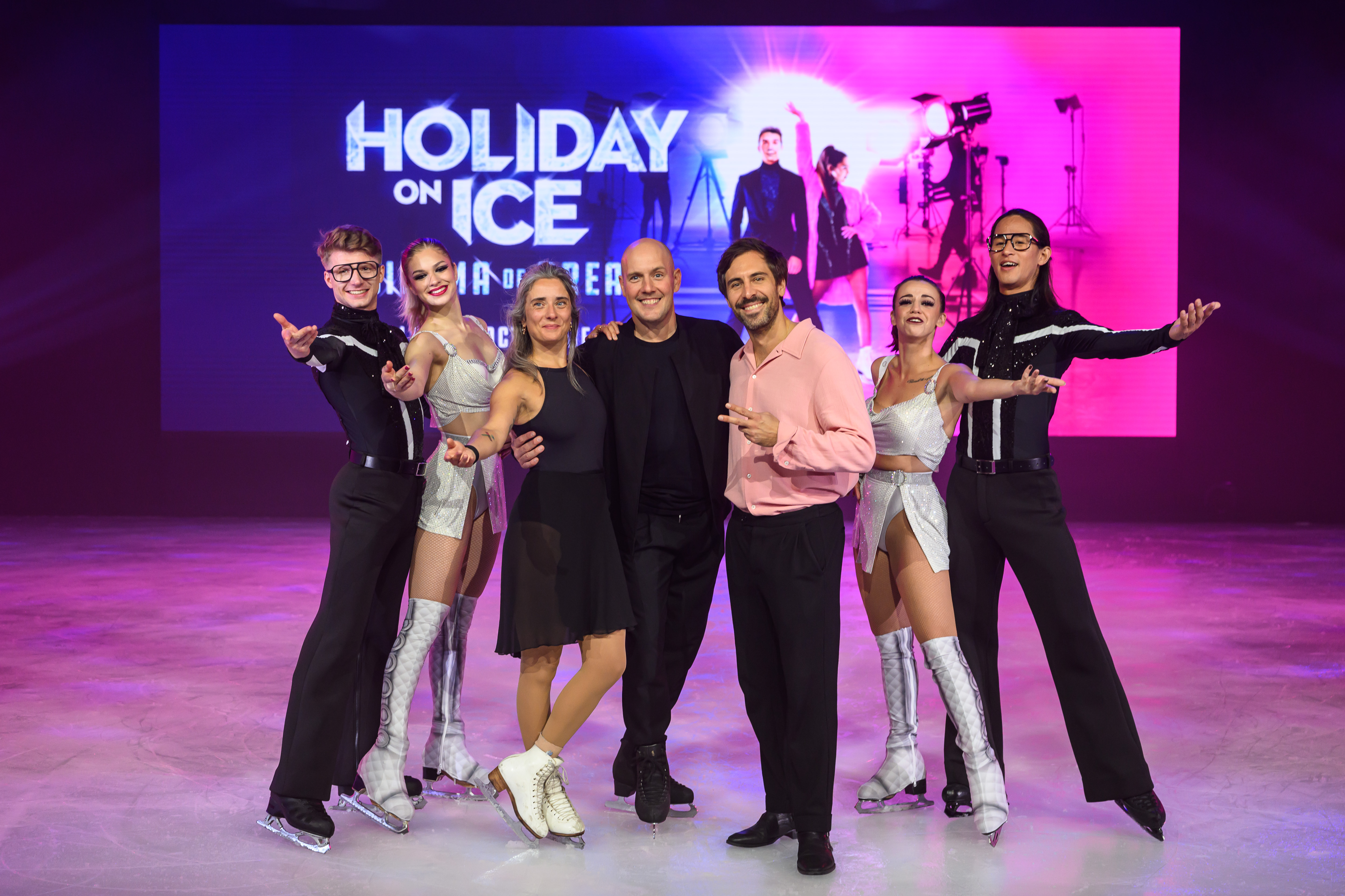 Eiskunstläuferinnen und Eiskunstläufer in Kostümen posieren auf einer Eisfläche vor Holiday on Ice-Bühnenhintergrund