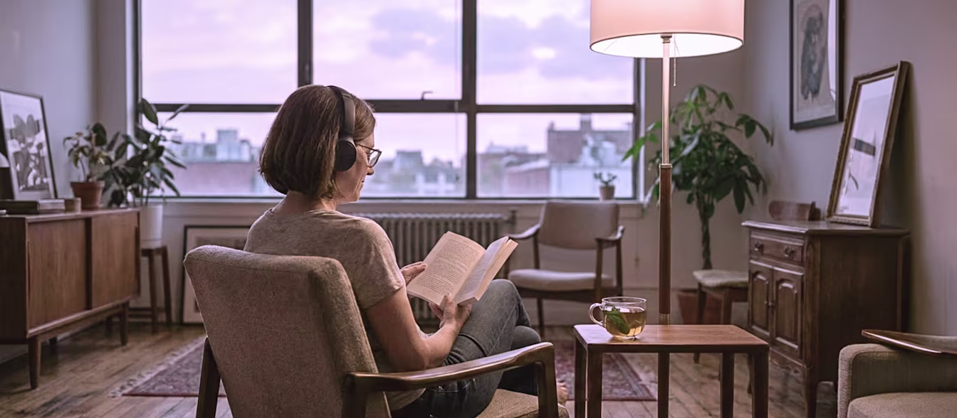 Frau liest in einem Sessel ein Buch und hört dabei Klassik zum Träumen