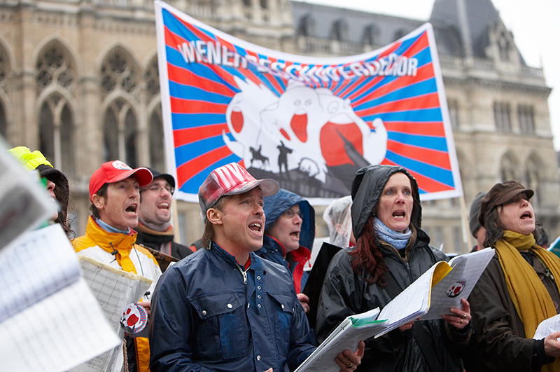 Menschen mit Liedblättern und Plakat singend vor dem Rathaus 