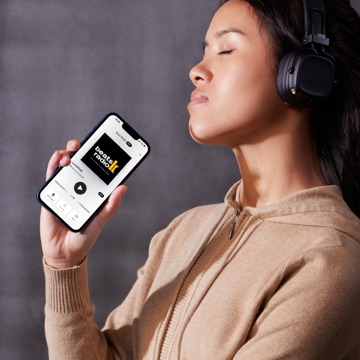 Beats Radio App im Handy, Frau hat Kopfhörer auf und hört den Sender