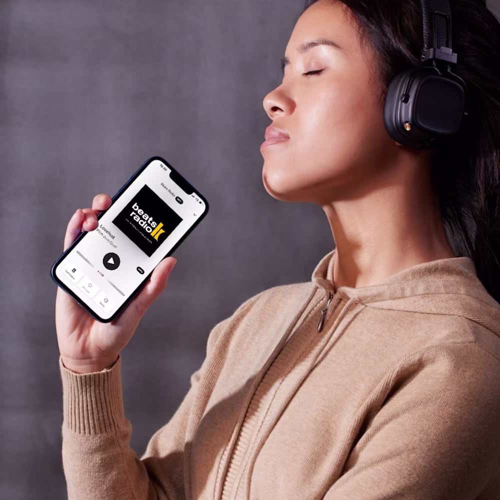 Beats Radio App im Handy, Frau hat Kopfhörer auf und hört den Sender