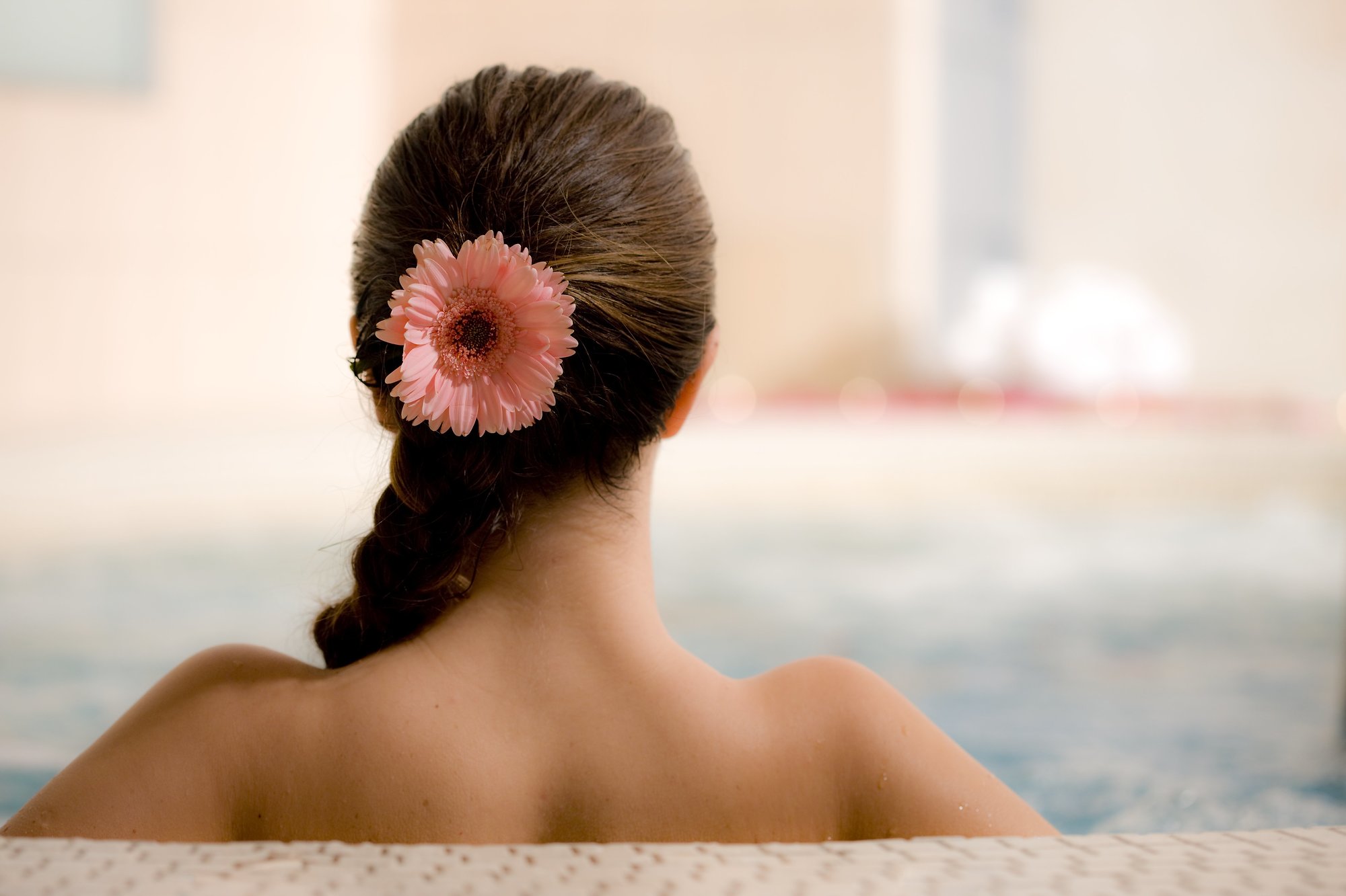 Frau mit geflochtenem Zopf und rosa Blume im Haar entspannt im Spa-Pool