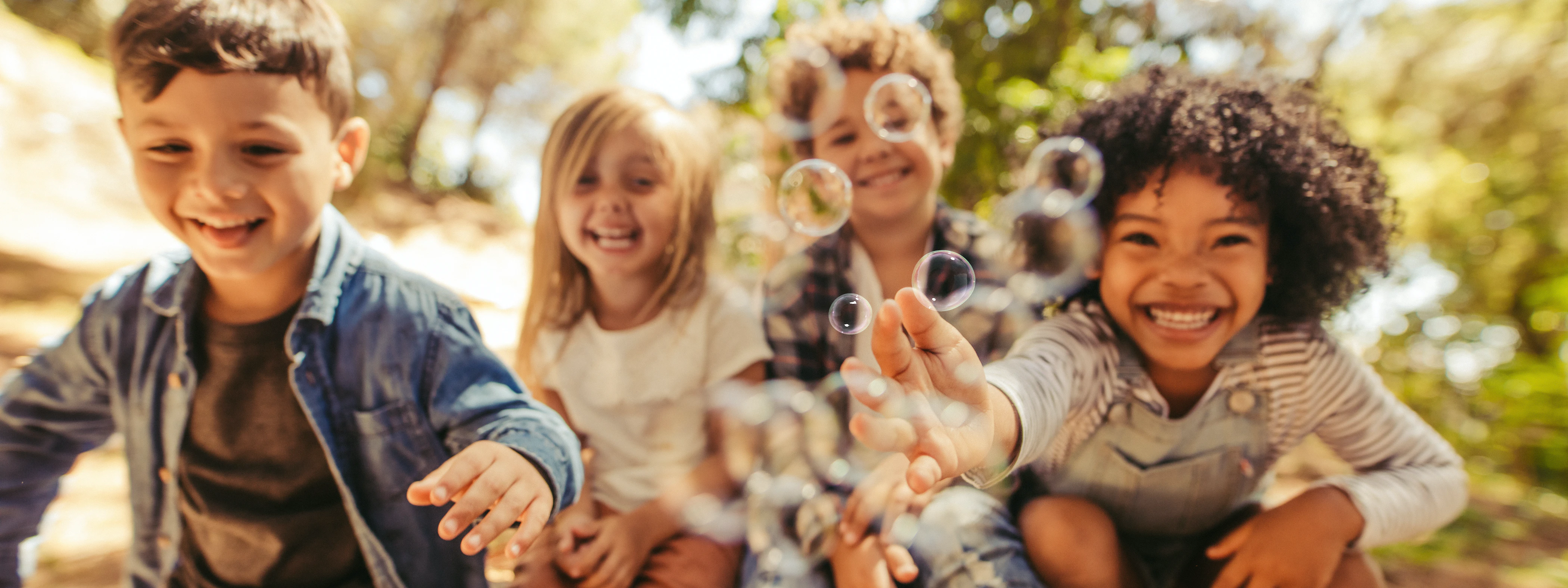 Vier verschiedene Kinder mit Seifenblasen, die Lachen