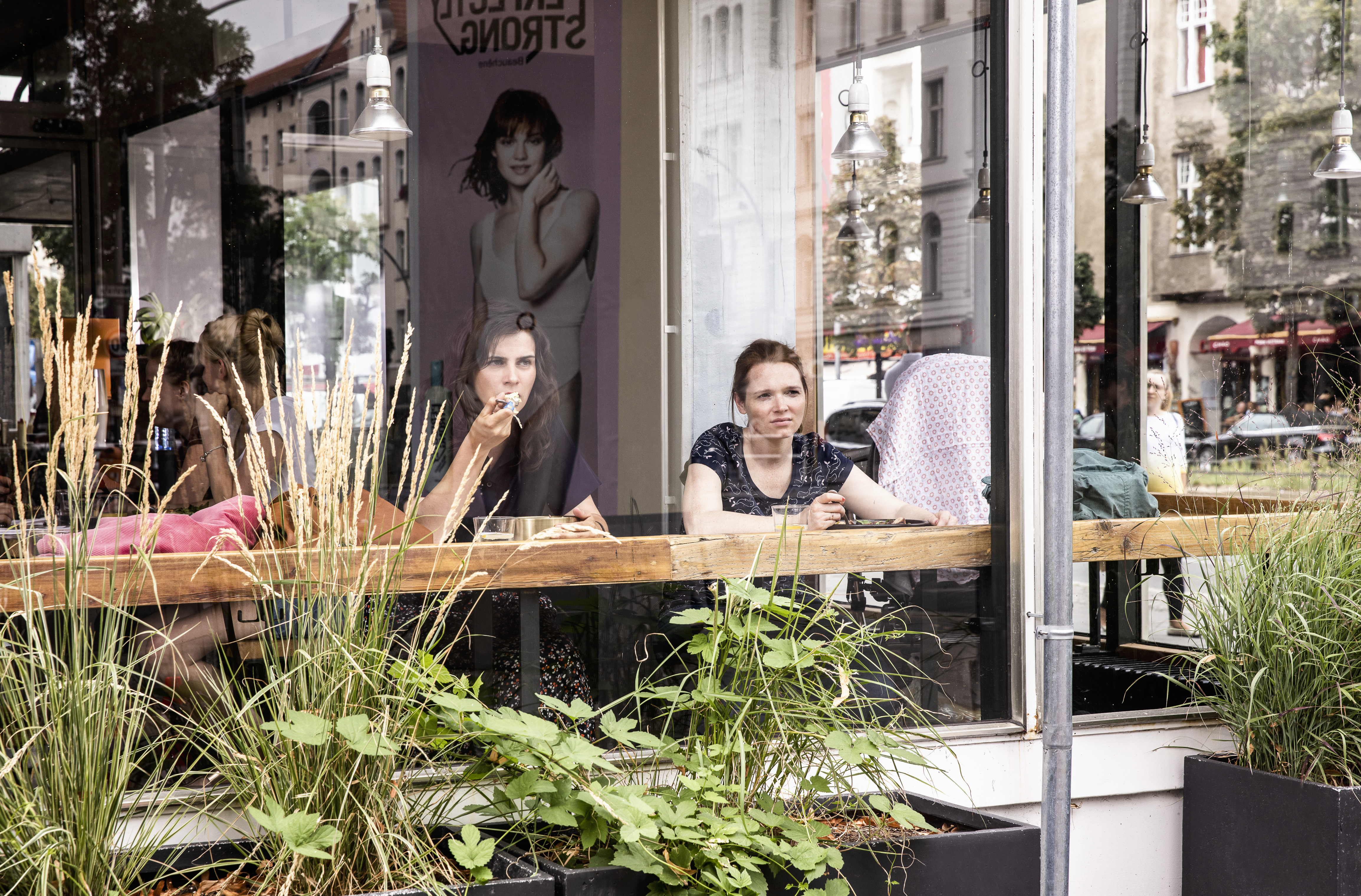 Nora Tschirner und Karoline Herfurth sitzen hinter einer Scheibe in einem Café