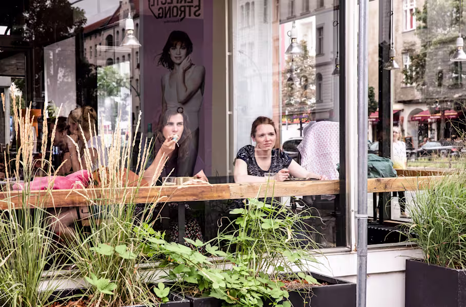 Nora Tschirner und Karoline Herfurth sitzen hinter einer Scheibe in einem Café