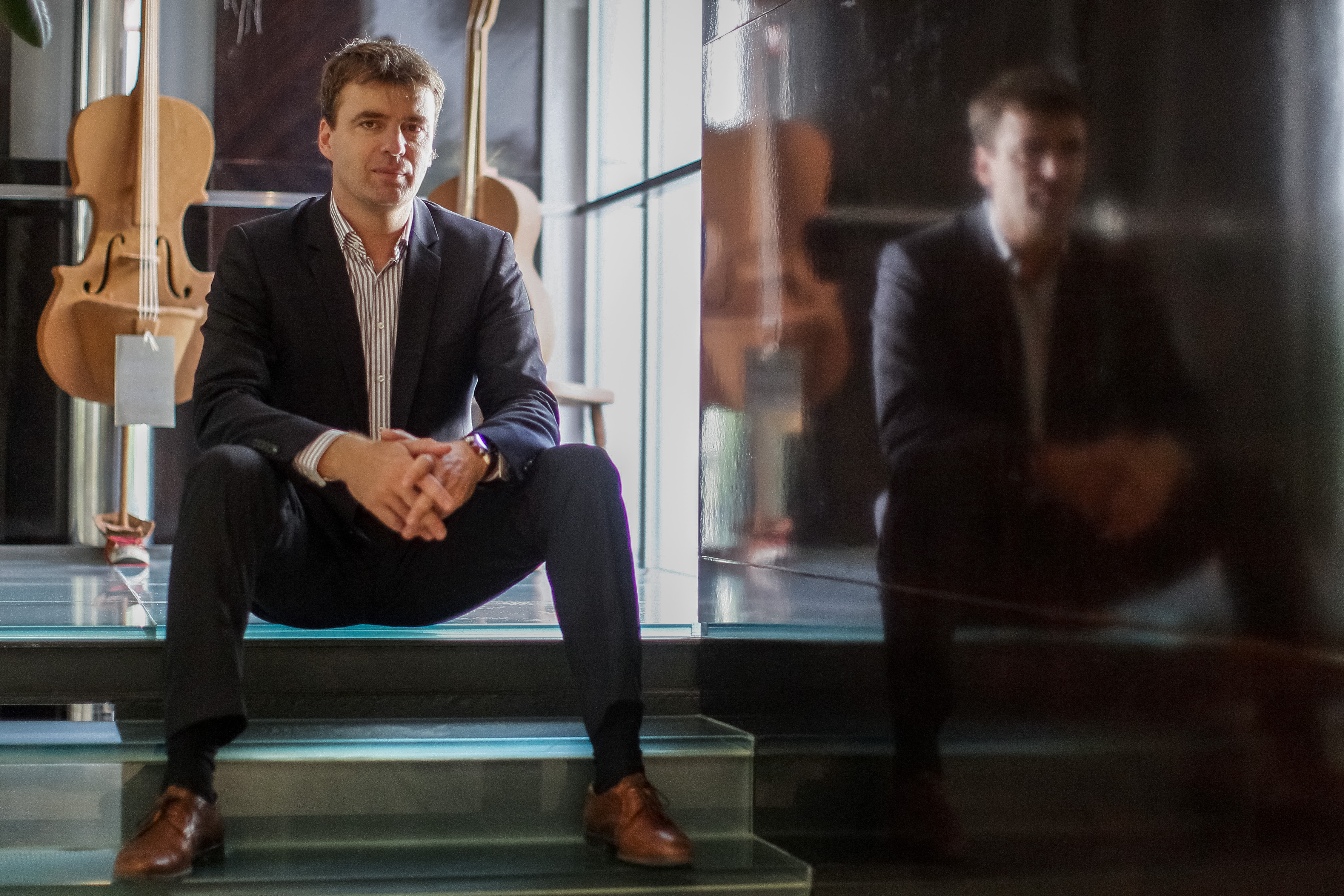 Dirigent Gabriel Feltz sitzt auf einer Treppe, im Hintergrund Geigen