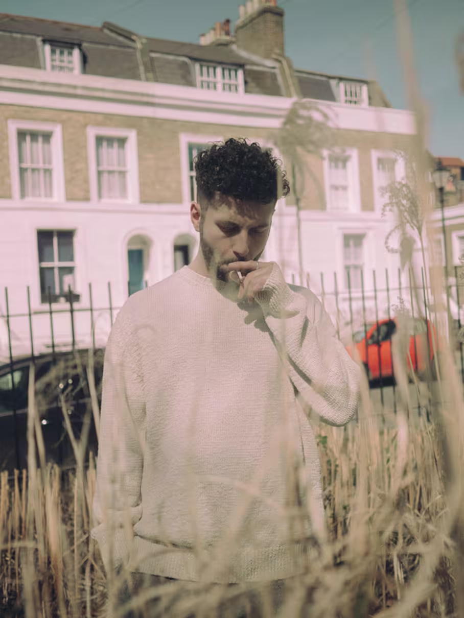 DJ Elderbrook steht in einem Feld vor einer Häuserreihe