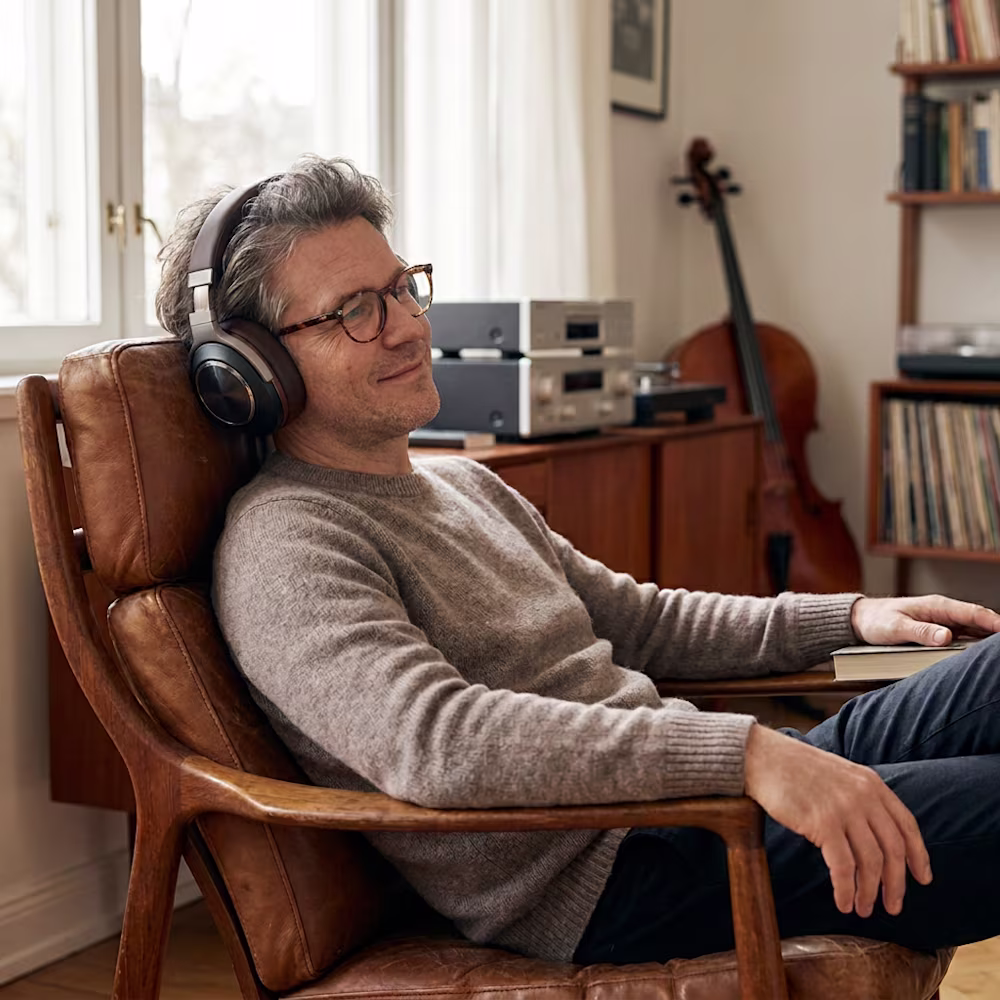 Ein Mann hört in seinem Sessel mit Over-Ear Kopfhörern klassische Musik.